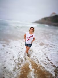 Smiling woman with hands in pockets standing on shore at beach