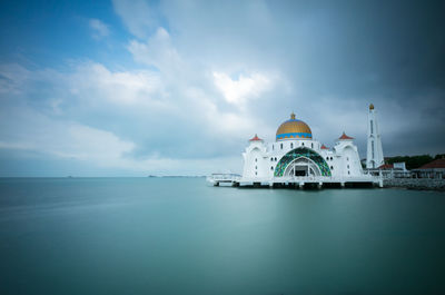 View of building by sea against cloudy sky