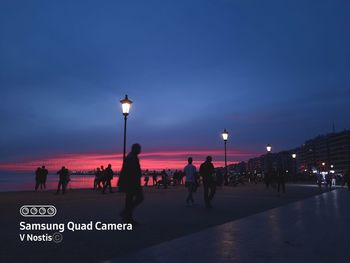 Silhouette people on street against sky during sunset