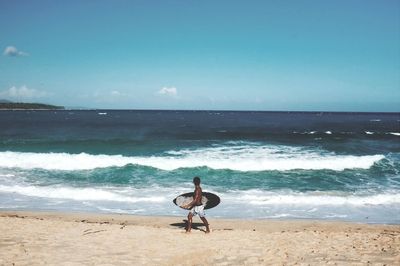 Man with surfboard walking on seashore at beach against sky