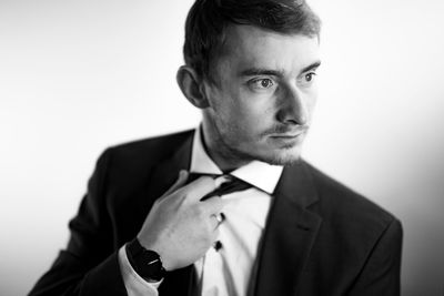 Close-up of businessman adjusting necktie against white background