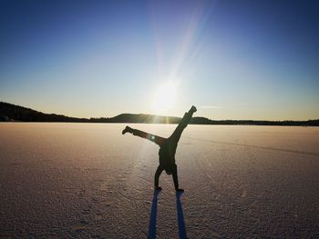 Man with arms outstretched against sky on sunny day