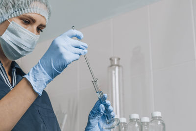 Woman in mask and rubber gloves in laboratory examines quality of water with glass tube filled 