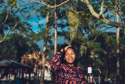 Portrait of smiling young woman standing against trees