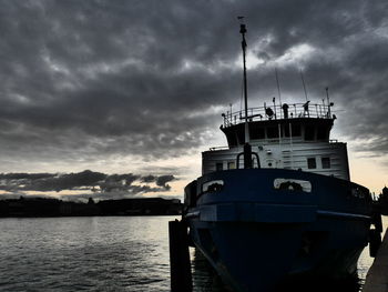 Ship moored at harbor against dramatic sky
