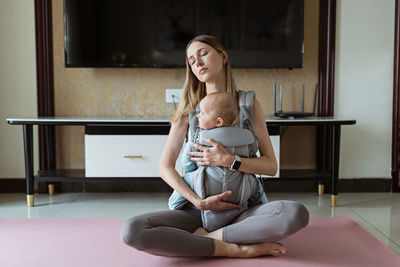 Mother embracing baby while sitting on exercise mat