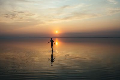 Silhouette person on sea against sky during sunset