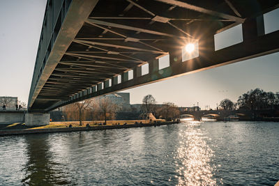 Bridge over river by illuminated buildings against sky in city