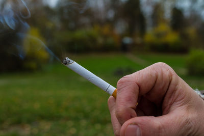 Cropped hand of man smoking cigarette at park