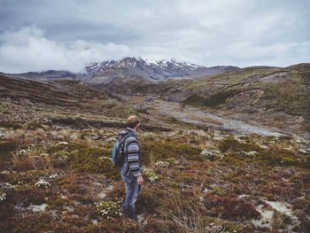 Side view of male hiker with backpack standing on mountain against cloudy sky