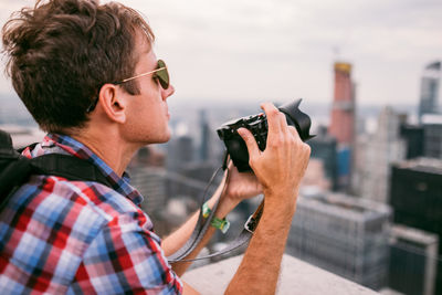 Portrait of young man photographing against sky in city