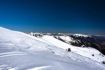 Glimpses of snow on monte grappa with blue sky and green trees, vicenza