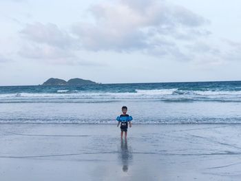 Boy wearing water wings while standing on shore against sky