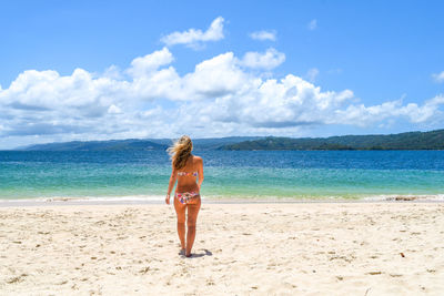 Rear view of bikini woman walking at sandy beach during sunny day