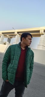 Young man looking away while standing against clear sky