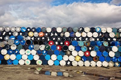 Stack of multi colored barrels against blue sky