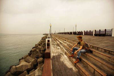 Man sitting on pier by sea against sky