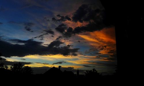 Silhouette houses against dramatic sky during sunset