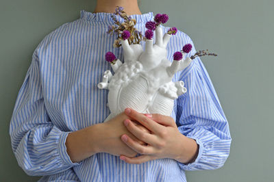 Midsection of woman holding artificial heart against white background