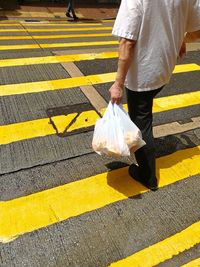 Low section of man with parcels walking on zebra crossing