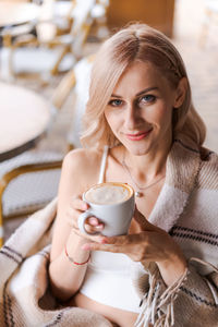 Portrait pretty blonde woman, smiling woman in cozy plaid, sitting in cafe