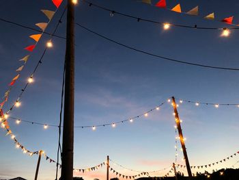 Low angle view of illuminated light bulbs against sky at sunset