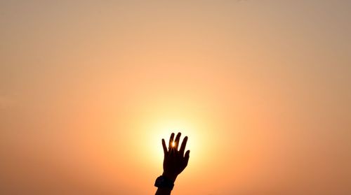 Silhouette person hand against orange sky during sunset
