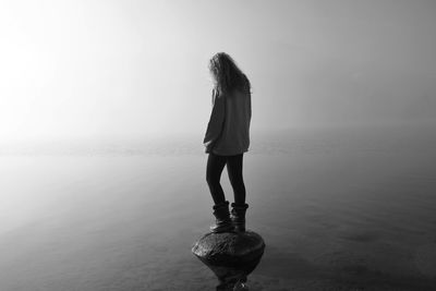 Rear view of woman standing on rock in lake