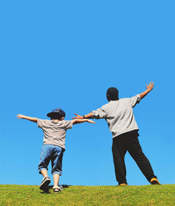 Rear view of father and son with arms outstretched standing against clear blue sky