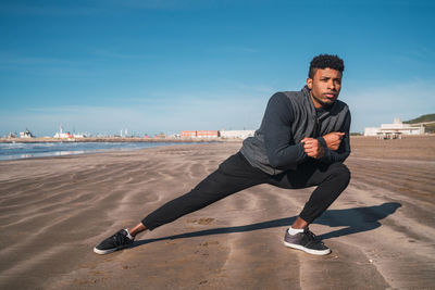 Young man exercising on beach against sky