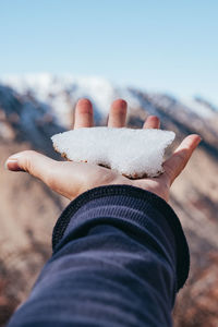 Cropped hand holding ice against clear sky