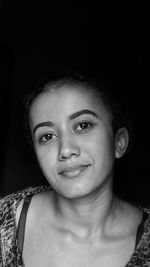 Portrait of smiling young woman against black background