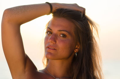 Close-up of beautiful woman with hand in hair during sunset