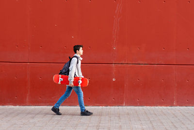 Full length of boy standing against red wall