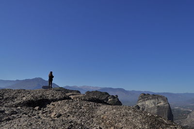 Woman standing on rocky mountains against clear blue sky