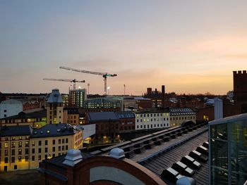 Construction site by buildings against sky during sunset