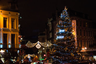 Illuminated christmas tree by building at night