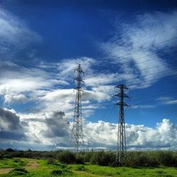 Electricity pylon on field against cloudy sky