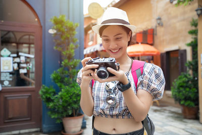 Smiling woman photographing with camera amidst buildings in city