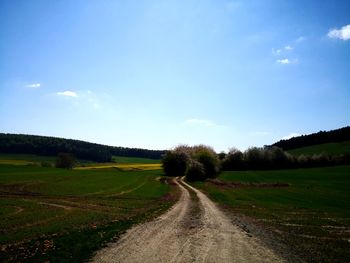 Dirt road amidst field against sky