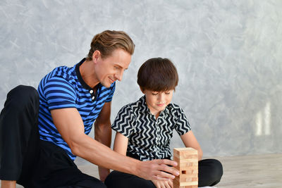 Father and son playing with block toys while sitting on floor at home
