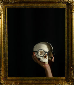 Close-up of man holding skull against black background seen from picture frame