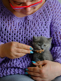 Portrait of a middle-aged woman feeding a cute kitten pate using a spoon 