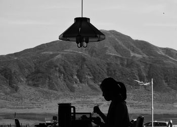 Silhouette woman eating food while sitting against mountains and sky