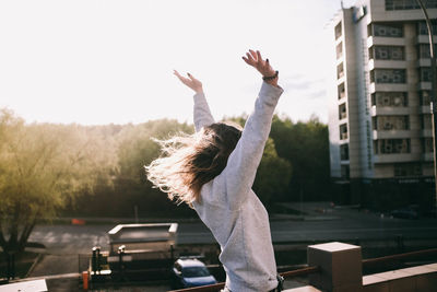 Woman with arms raised in city against sky