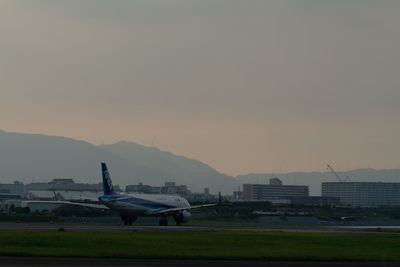 Airplane on airport runway against sky during sunset