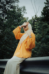 Woman wearing hijab sitting on railing against trees in forest