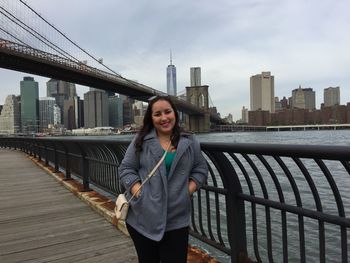 Portrait of young woman standing on bridge against cityscape