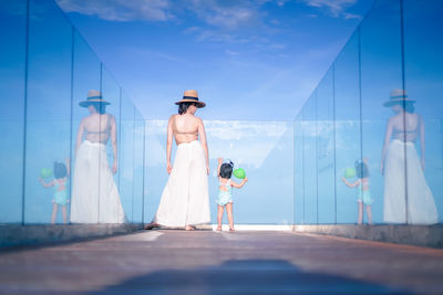 Rear view of woman standing with daughter against sky