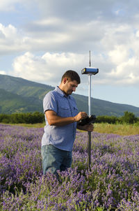 Surveyor with theodolite on lavender field against sky